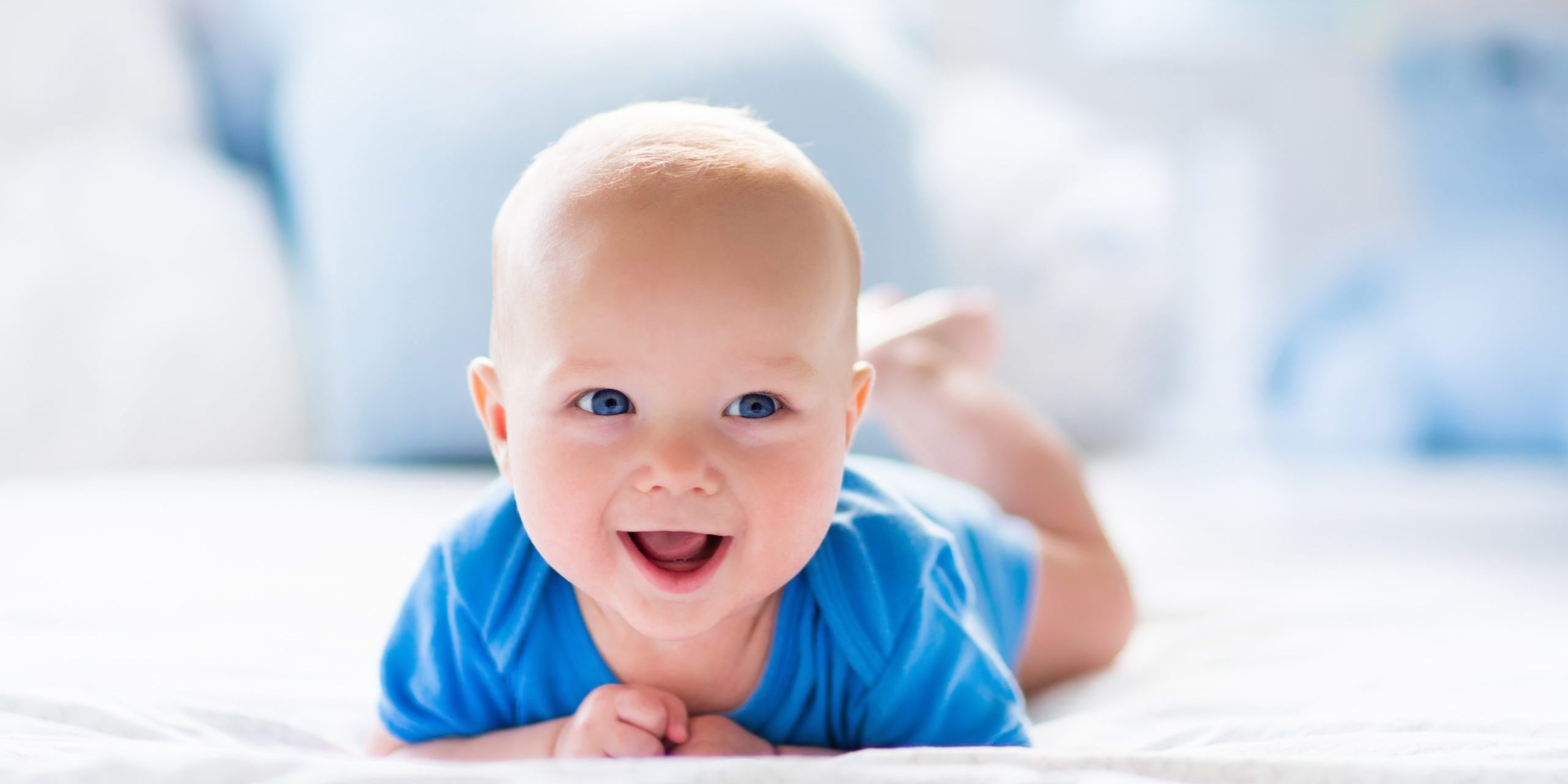 Adorable baby boy in white sunny bedroom. Newborn child relaxing in bed. Nursery for young children. Textile and bedding for kids. Family morning at home. New born kid during tummy time with toy bear.